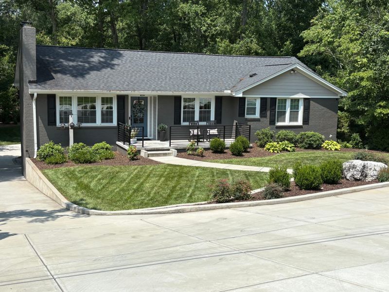 A grey ranch home with new shrub beds, stone bed edging, and a freshly cut striped front lawn